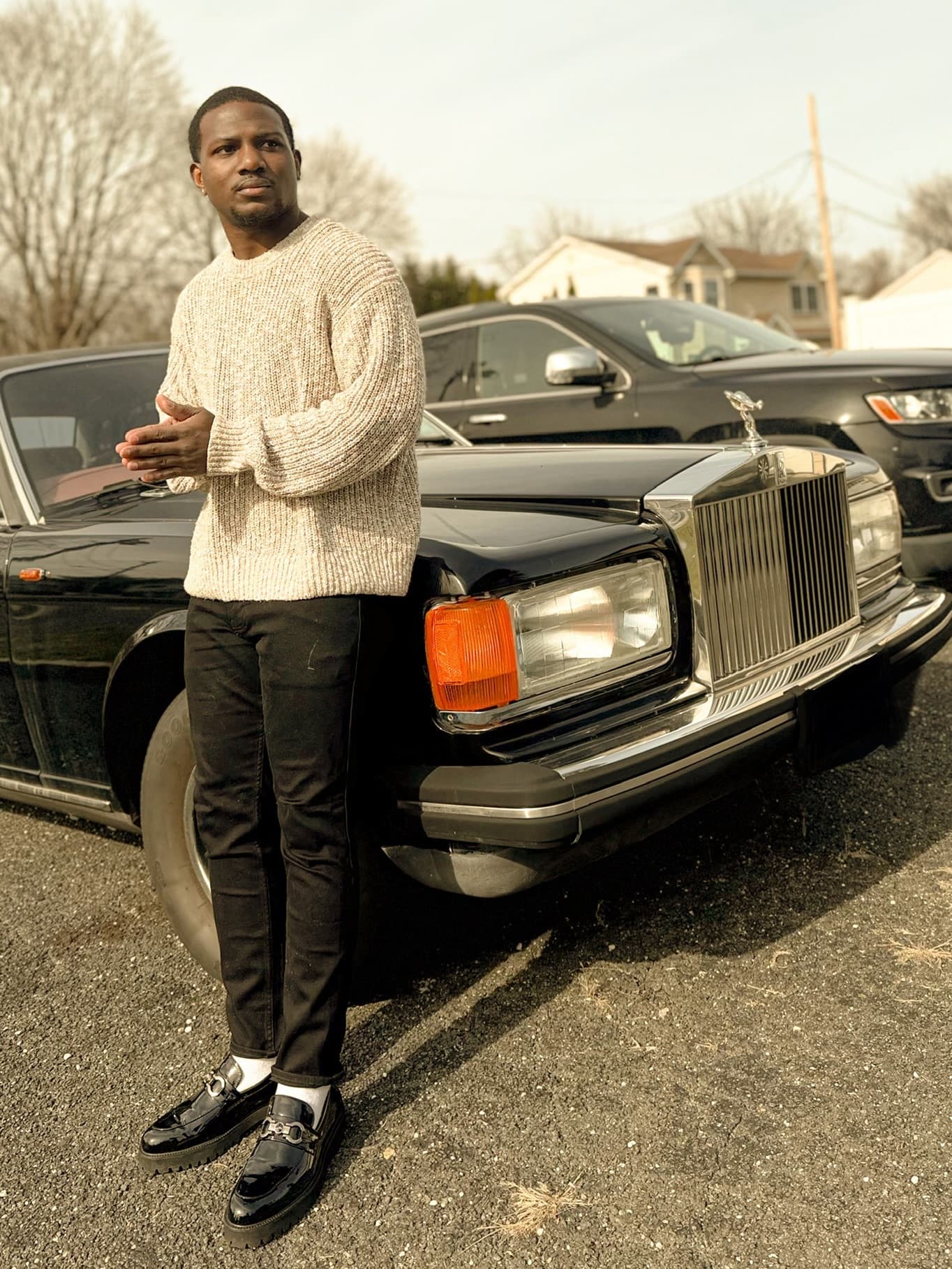 Kenneth Sene in a cream knit sweater standing beside a black Rolls-Royce